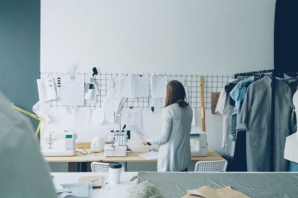 Designer trabalhando em um ateliê contemporâneo, cercado por máquinas de costura e projetos de roupas.