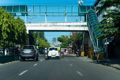 Passarela de pedestres sobre uma avenida urbana com veículos e circulação de pessoas.