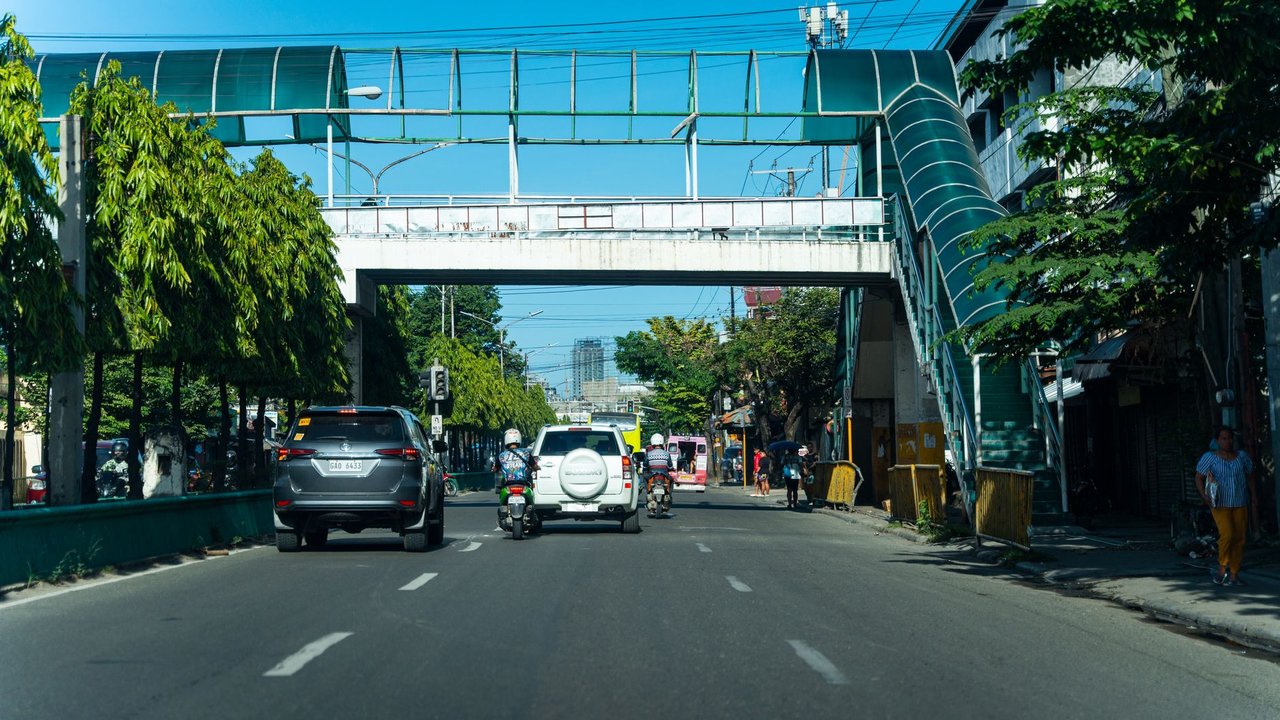 Passarela de pedestres sobre uma avenida urbana com veículos e circulação de pessoas.