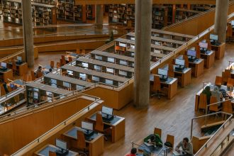 Interior amplo de biblioteca, com mesas de estudo e computadores disponíveis aos usuários.